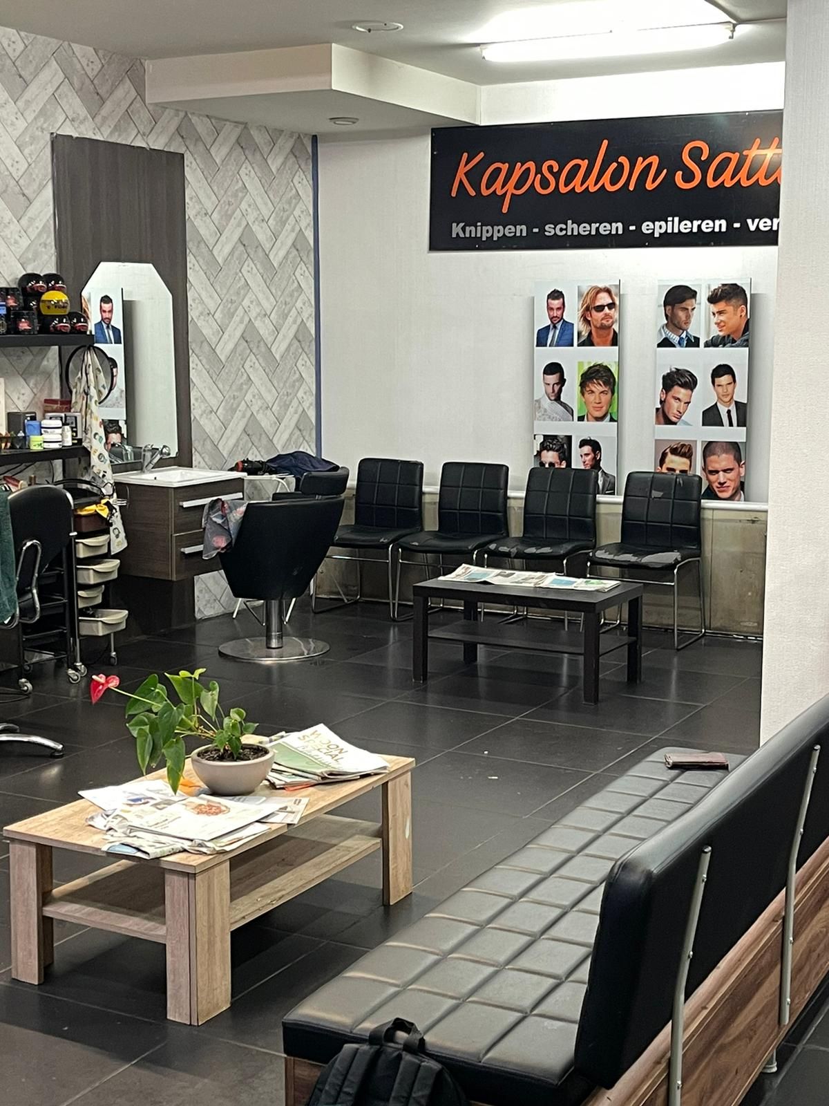 De wachtruimte met bank, tafel en kapselfoto's aan de muur