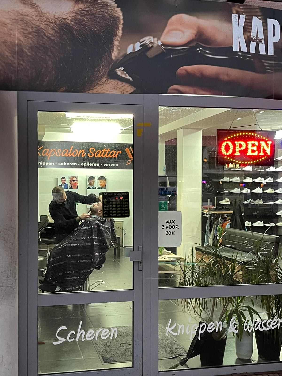 Het raam van de salon met het bord OPEN en de belettering Scheren en Knippen en wassen