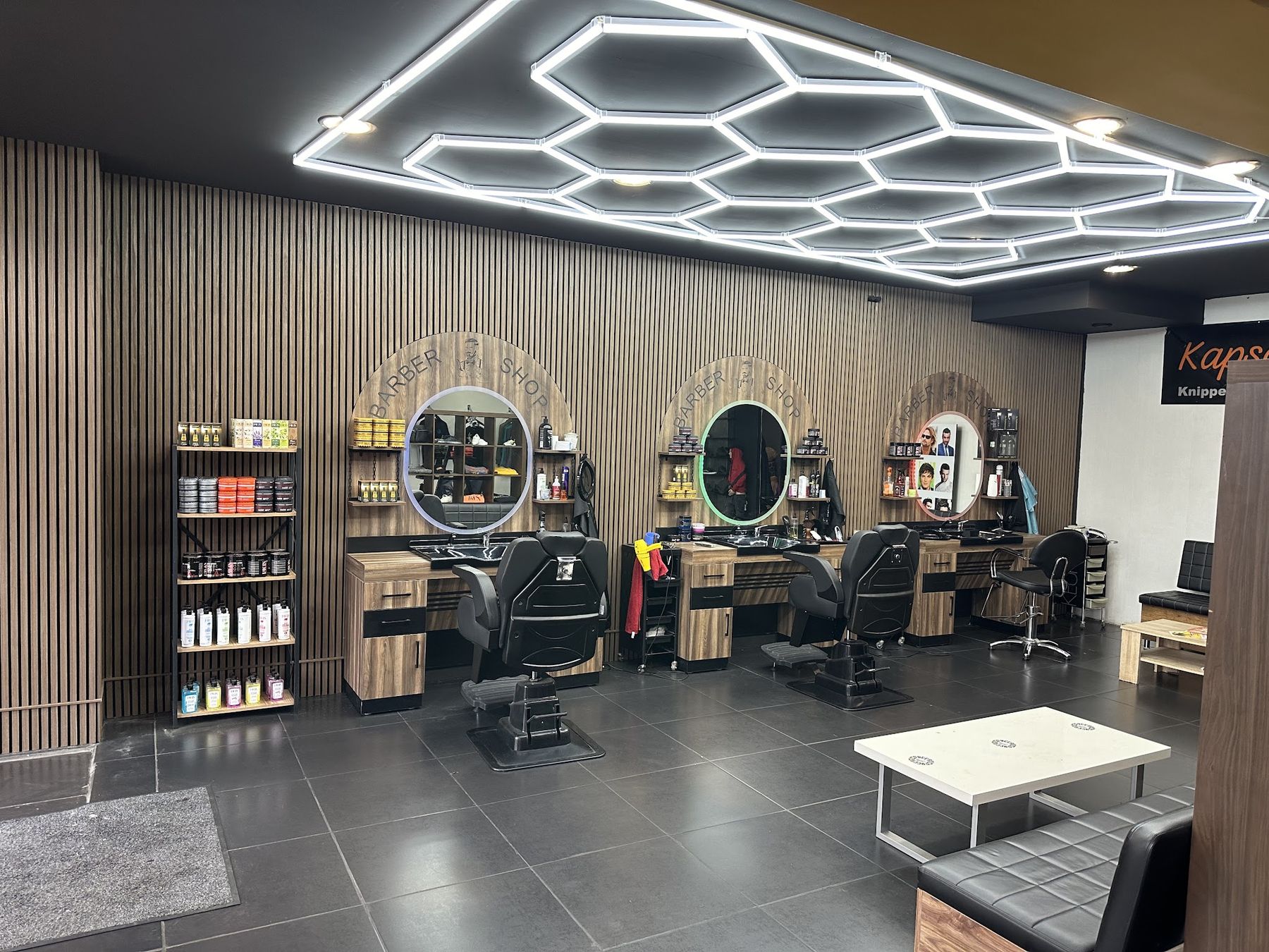 De salon van Kapsalon Sattar: een zeshoekig lichtplafond, houten lamellen, ronde spiegels en drie kappersstoelen